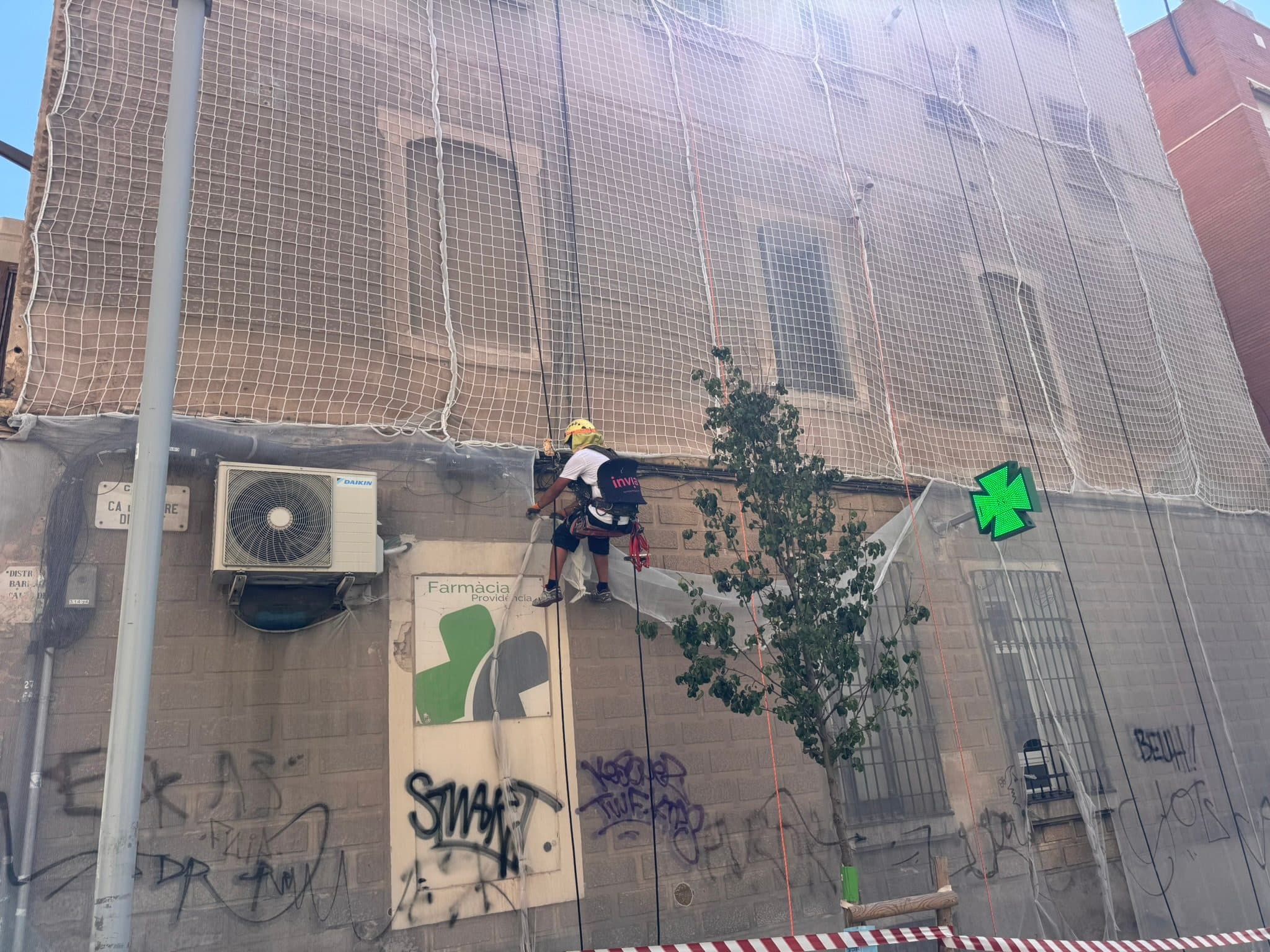 Operario colgado de cuerdas instalando una red de protección en la fachada de un edificio de viviendas