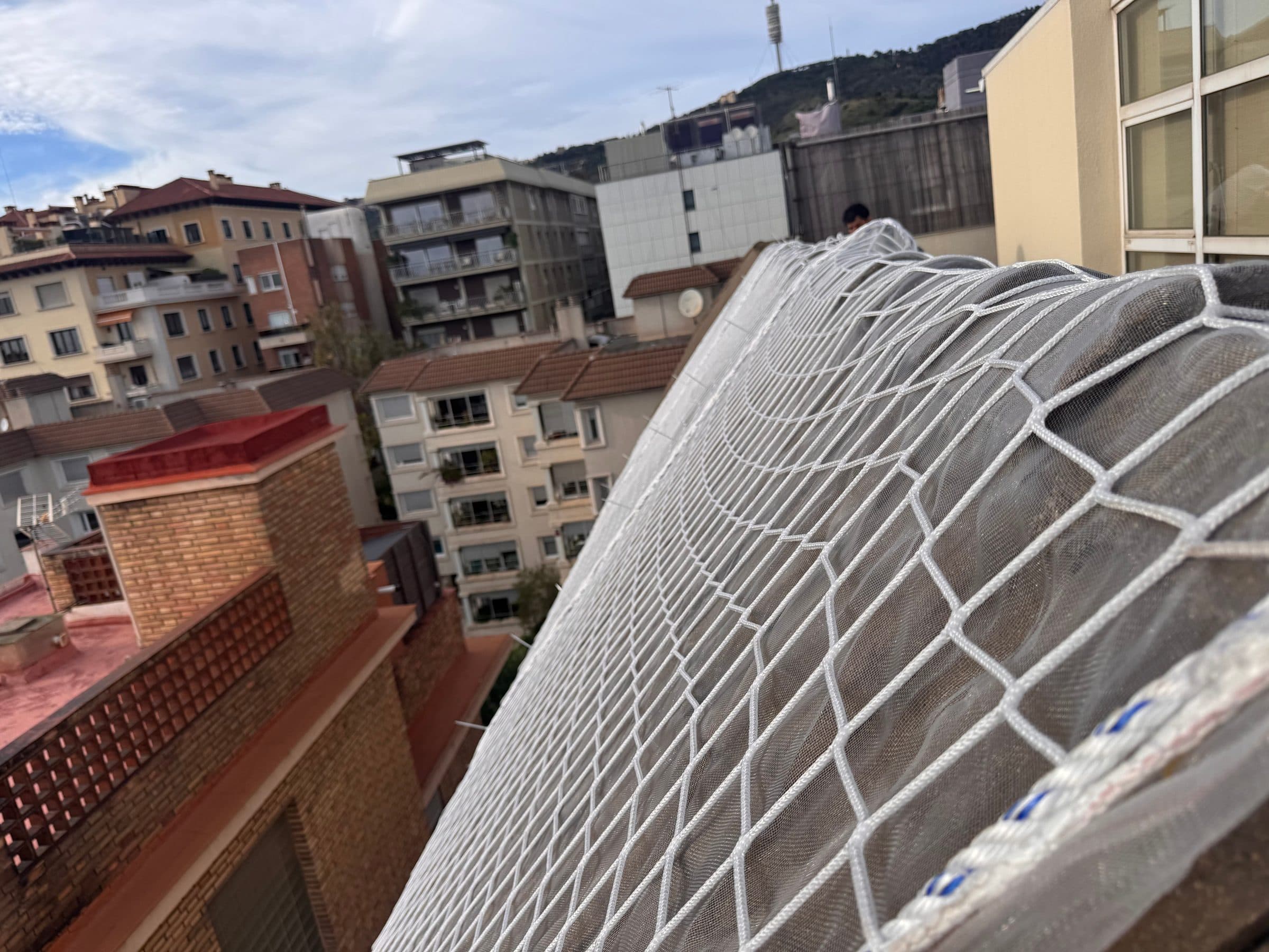 Red de seguridad blanca sobre una cubierta muy inclinada, con edificios de viviendas y montañas al fondo