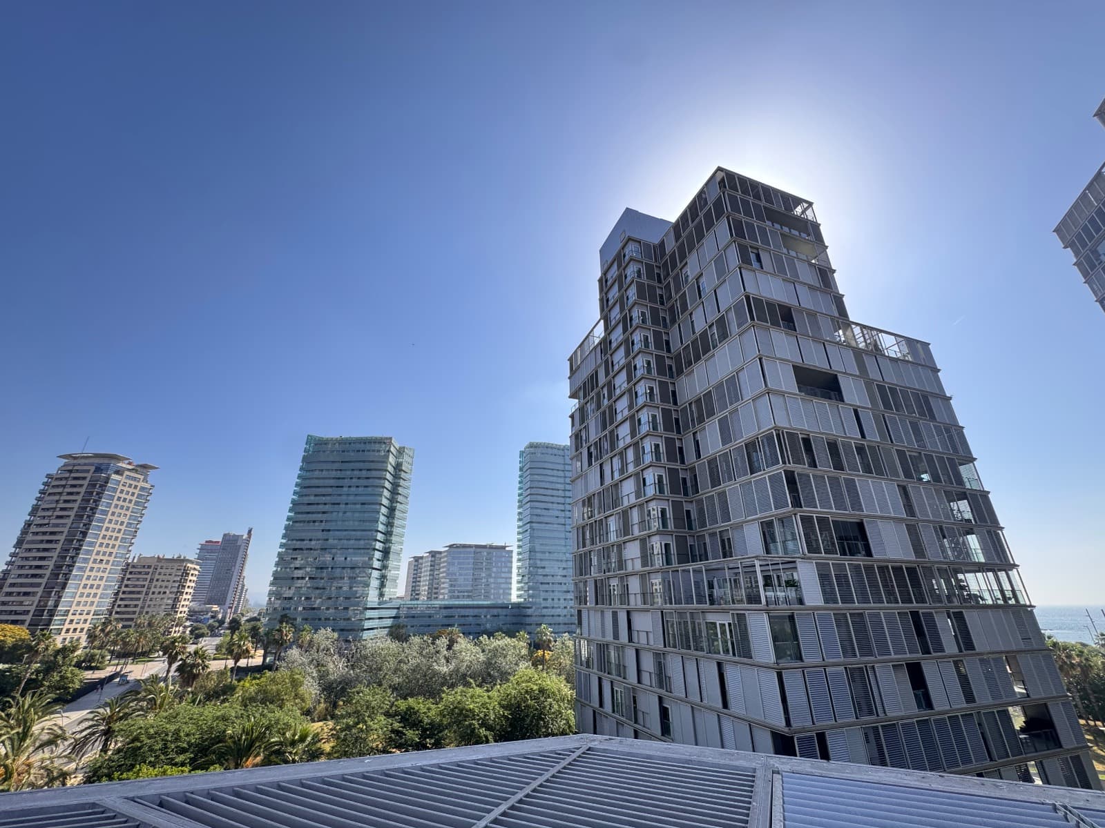 Edificio de lamas metálicas de la Vila Olímpica visto desde una cubierta, con torres al fondo
